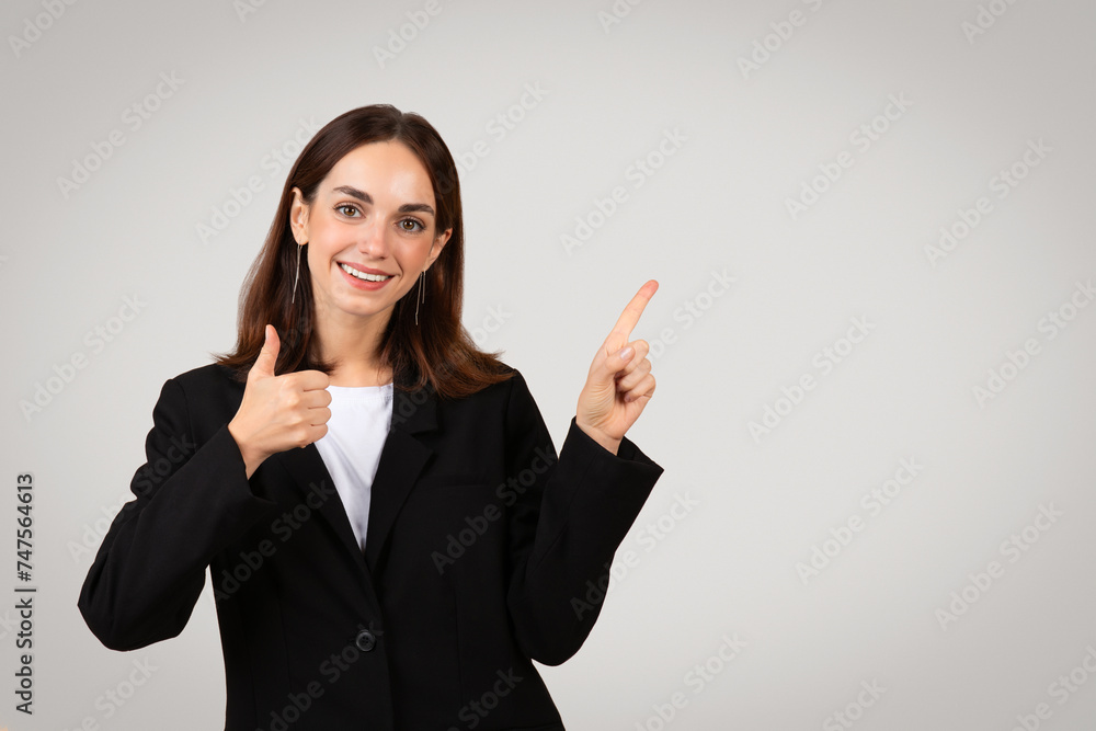 Cheerful businesswoman in a black blazer gives a thumbs up and points with her other hand Cheerful businesswoman in a black blazer gives a thumbs up and points with her other hand