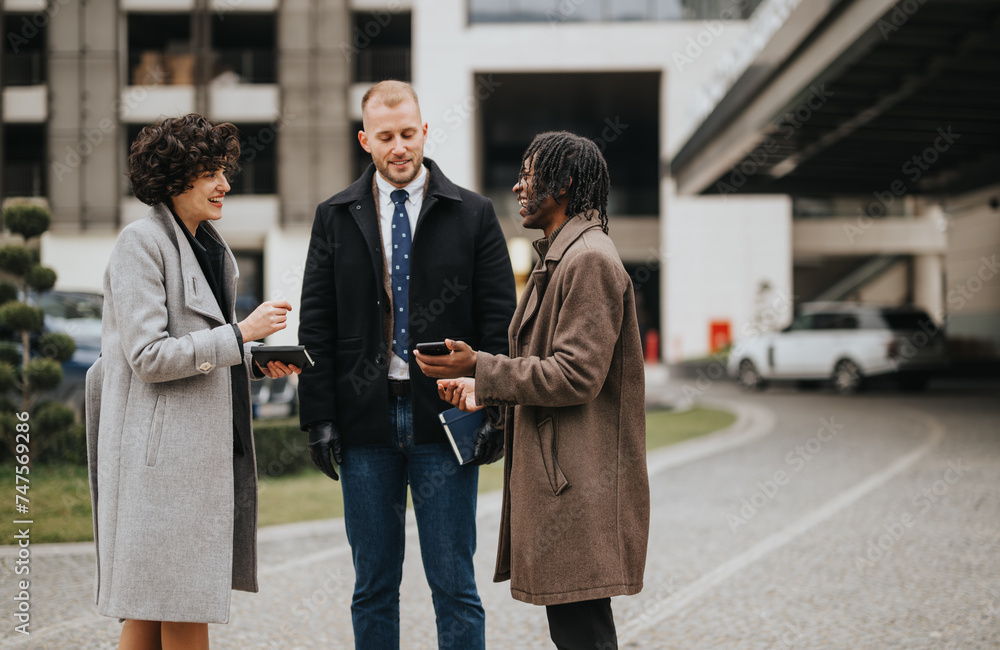 A diverse group of young professionals engaging in a friendly conversation with mobile devices outside a modern office building.