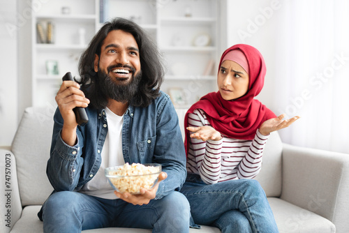 Angry muslim woman looking at husband watching tv at home