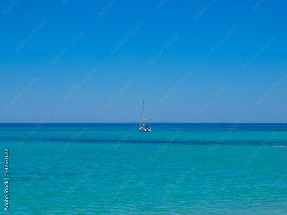 Sailboat in the horizon line between turquoise waters and clear blue sky Sailboat in the horizon line between turquoise waters and clear blue sky
