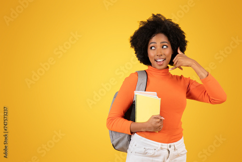 Amused young woman with afro hair, in an orange sweater and white pants