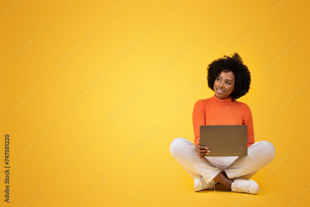 Content young African American woman with curly hair sitting cross-legged holding a laptop Content young African American woman with curly hair sitting cross-legged holding a laptop
