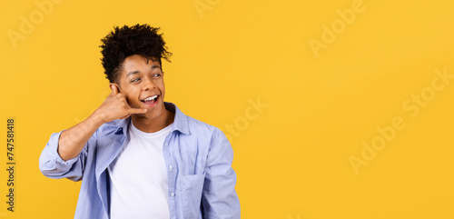 Joyful black guy making call me gesture against yellow background photo