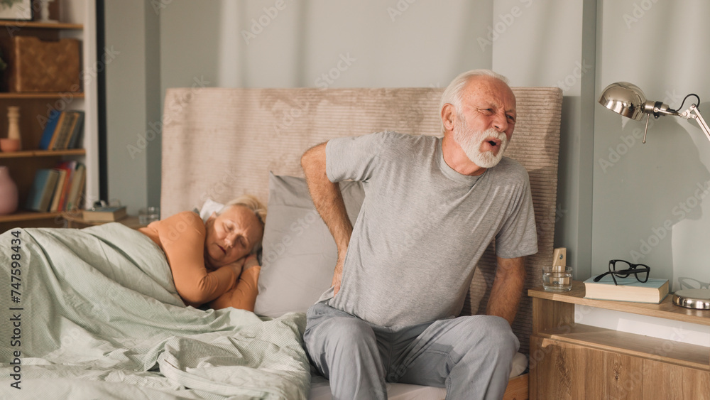 Senior man having a backpain while waking up next to his wife
