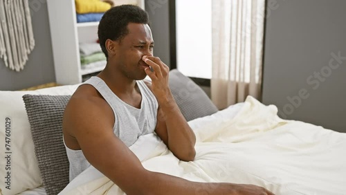 Unhappy young african american man in pyjamas, disgusted by intolerable stinky smell in bedroom, holding breath and nose amidst the repulsive stench. photo