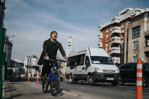 Focused male city commuter riding a bicycle on an urban road with vehicles in the background during the day.