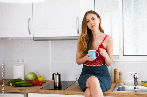 Portrait of an attractive young girl with cup of coffee in the home kitchen