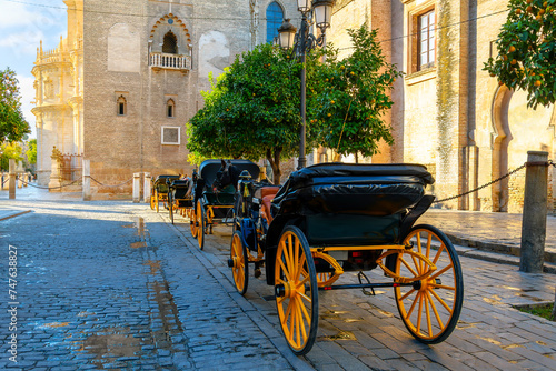 A row of empty horse drawn carriages with their traditional yellow wheels line up waiting for tourists in the morning by the cathedral, in the Andalusian city of Seville, Spain.