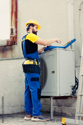 Experienced repairman contracted to recondition external air conditioner starting task. Qualified engineer wearing protective gear preparing to mend malfunctional outdoor hvac system