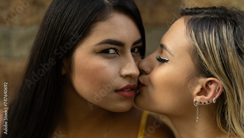 Sensual closeup portrait of two multiracial girls kissing while one of them sees the camera