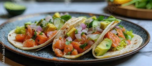 A plate displays three homemade salmon tacos with onion, cucumber, and avocado, placed on a table.