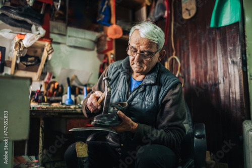 A senior cobbler is fixing shoes at his small workshop. © Zamrznuti tonovi