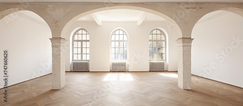 An empty room in a renovated old house  featuring arched doorways and large windows that allow natural light to filter in. The room is spacious with white walls  creating a bright and airy atmosphere.