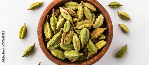 This top-view photograph showcases a wooden bowl filled with green cardamom seeds, isolated on a white background.