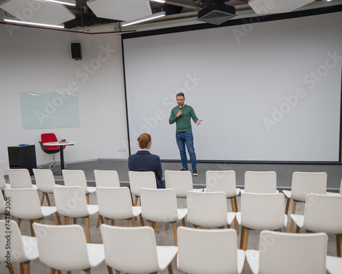 A red-haired Caucasian businesswoman sits in the front row of an empty conference room. Bearded man giving a lecture.  photo