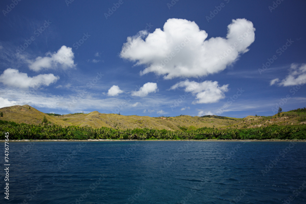 A view of Umatac Bay, Guam from the Pacific Ocean on a clam day with fluffy clouds in the blue sky