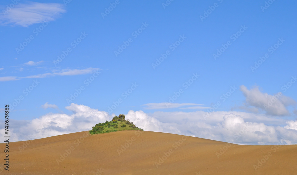 Small fallow hill in the undulating Tuscan fields with blue sky and white clouds on a spring day in the Crete Senese in Tuscany, Italy Small fallow hill in the undulating Tuscan fields with blue sky and white clouds on a spring day in the Crete Senese in Tuscany, Italy