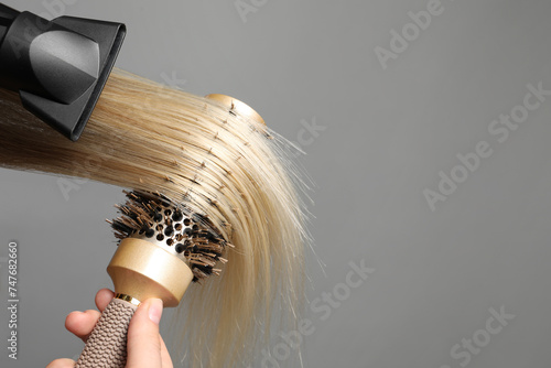 Hairdresser blow drying client's hair on light grey background, closeup. Space for text photo