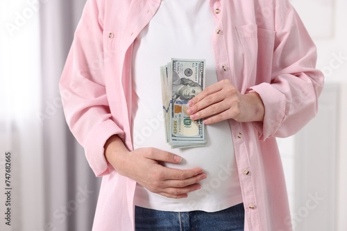 Surrogate mother. Pregnant woman with dollar banknotes indoors, closeup