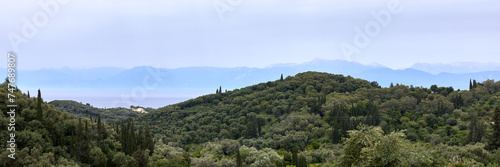 Green hills on the seashore and the silhouettes of the mountains on the horizon. View from the Greek island of Corfu to the mountains on the coast of Albania