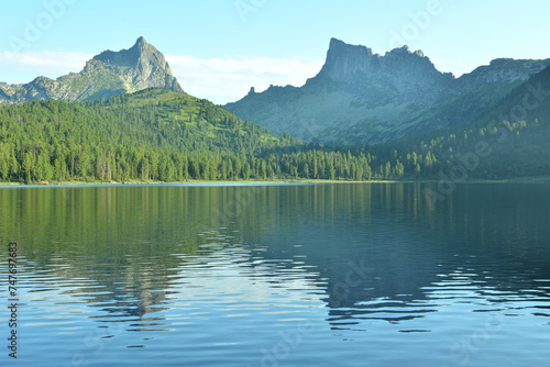 Reflection of two high pointed rocks in a large lake with shores covered with a dense cedar forest, on a sunny summer day.