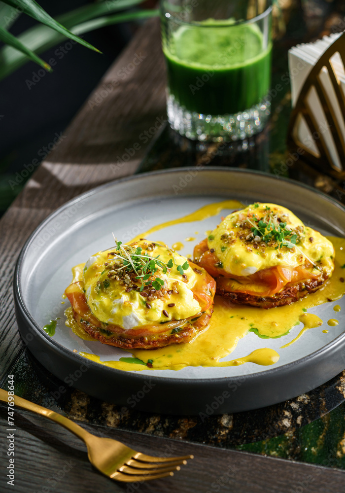 Delicious pancake with slice of salmon, eggs Benedict or poached eggs and sesame and microgreens on plate on marble table with smoothie. Healthy breakfast food, diet, top view Delicious pancake with slice of salmon, eggs Benedict or poached eggs and sesame and microgreens on plate on marble table with smoothie. Healthy breakfast food, diet, top view