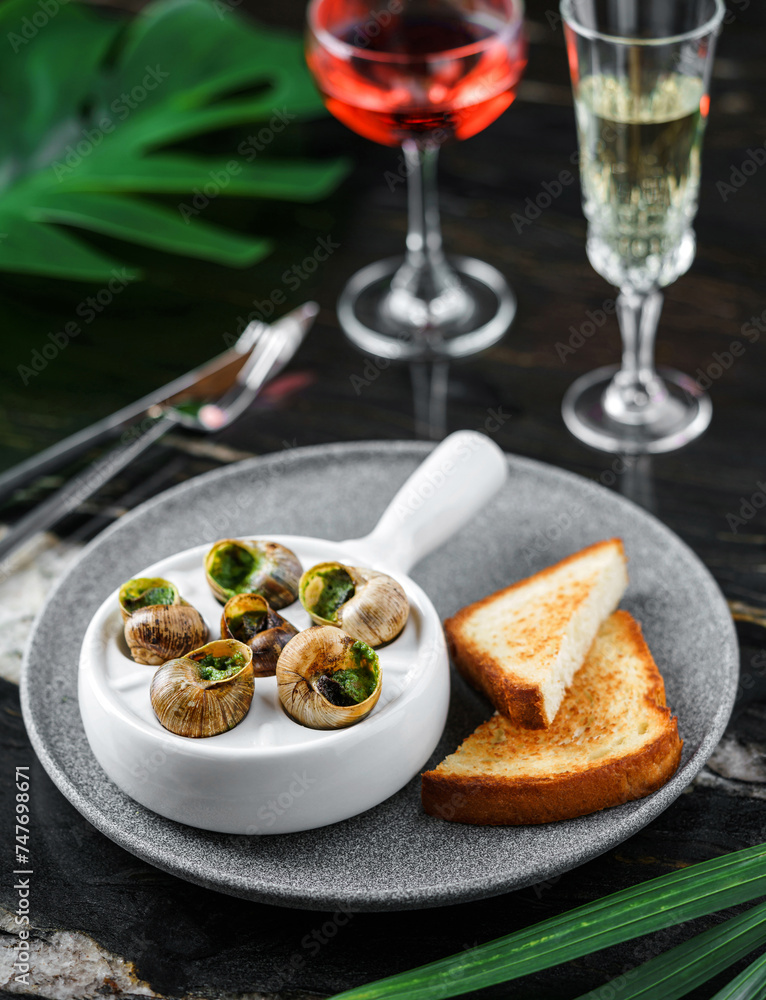Delicious sea snails with herbs and bread on plate over marble background with drinks. Gourmet food. Escargot Snails, top view