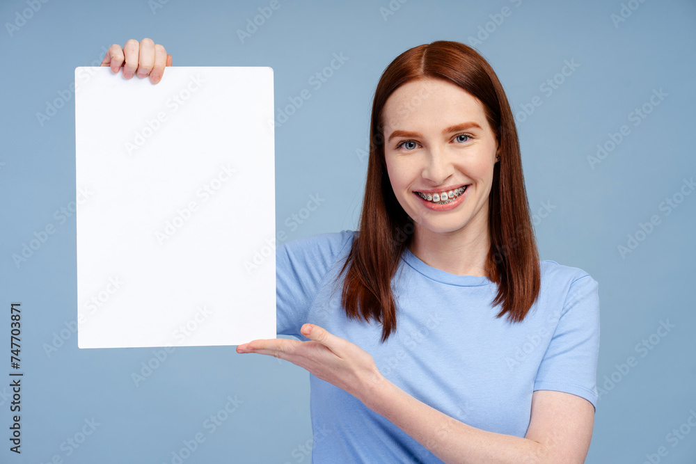 Smiling redhead, strikingly beautiful, demonstrating a placard, isolated on a blue background Smiling redhead, strikingly beautiful, demonstrating a placard, isolated on a blue background