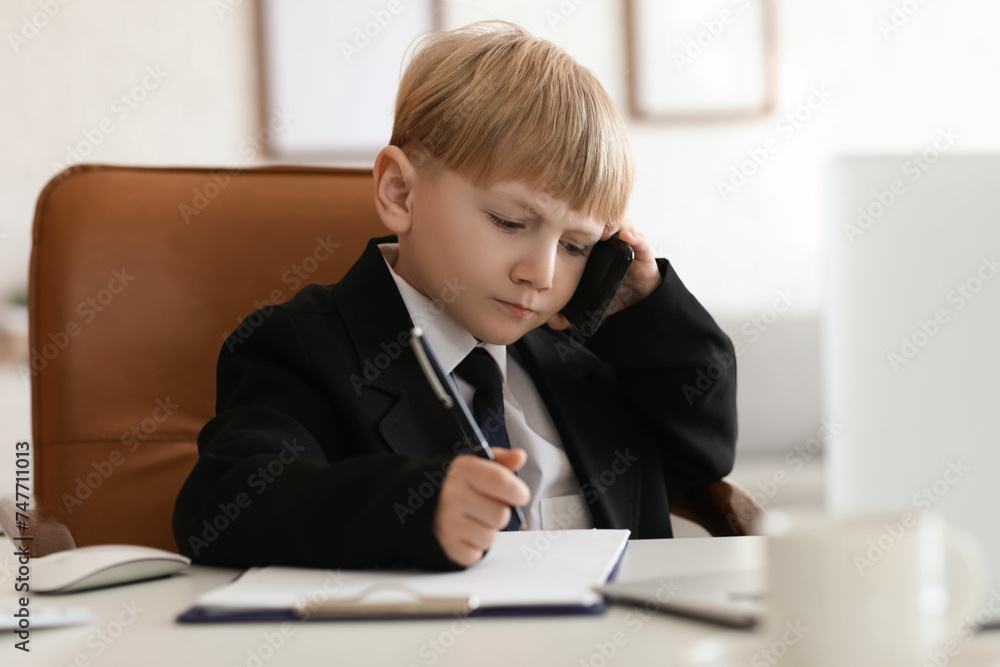 Funny little businessman talking by mobile phone at table in office Funny little businessman talking by mobile phone at table in office