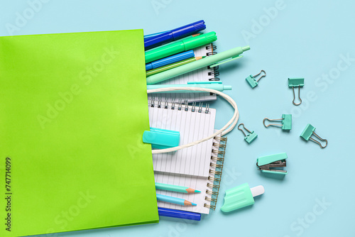 Green shopping bag with different school stationery on blue background