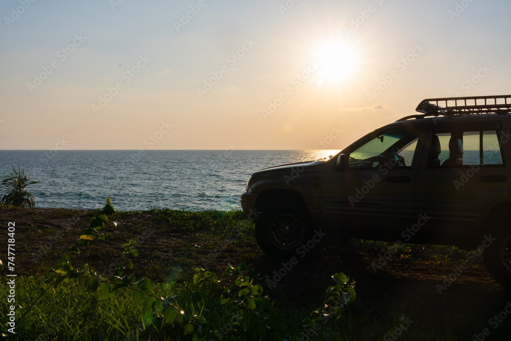 Fototapeta premium Phuket Thailand January 22,2024:Brown American SUV Jeep Grand Cherokee WJ 2002 on the beach sunset sky background in Phuket island Thailand,Travel and camping concept transportation background