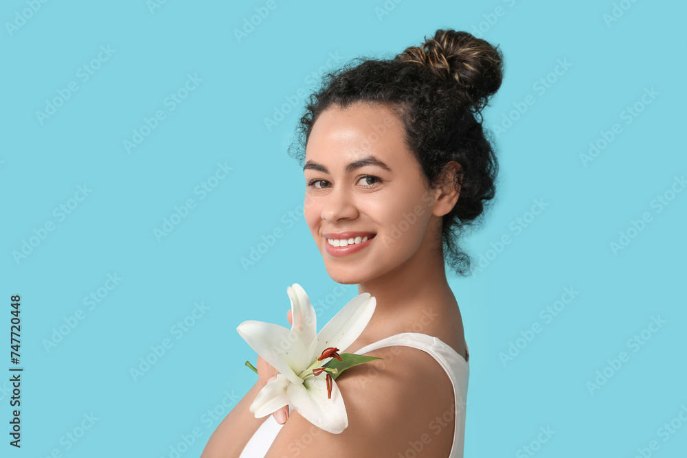 Beautiful young African-American woman with lily flower on blue background Beautiful young African-American woman with lily flower on blue background