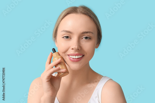 Beautiful young woman with bottle of cosmetic oil on blue background