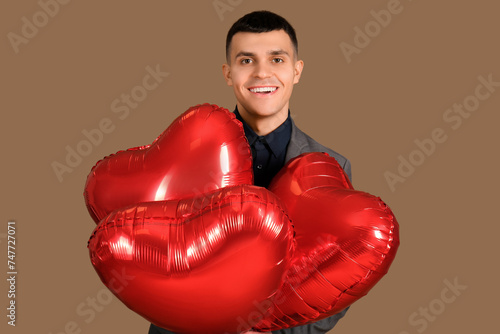 Handsome young man with heart-shaped air balloons for Valentine's day on brown background © Pixel-Shot
