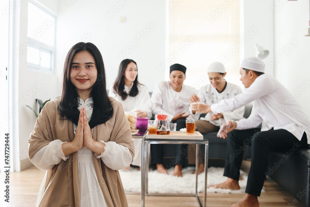 Beautiful young muslim girl showing greeting or welcoming gesture during Eid Mubarak celebration with her friends gather on the background Beautiful young muslim girl showing greeting or welcoming gesture during Eid Mubarak celebration with her friends gather on the background