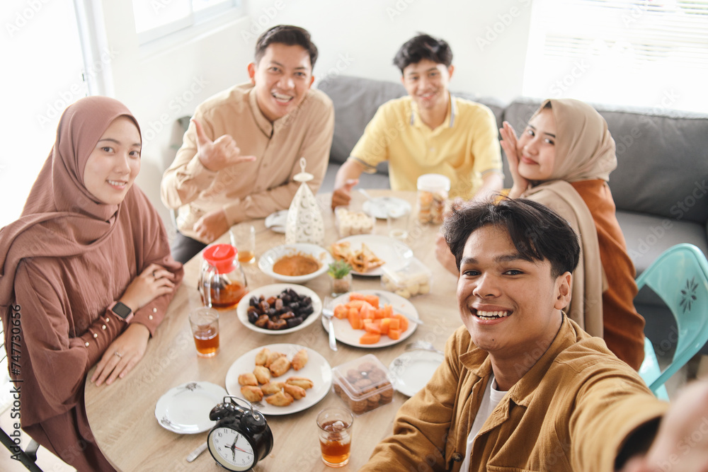 Group of Asian muslim man and woman taking selfie on dining table during dinner and hangout together on iftar ramadan 