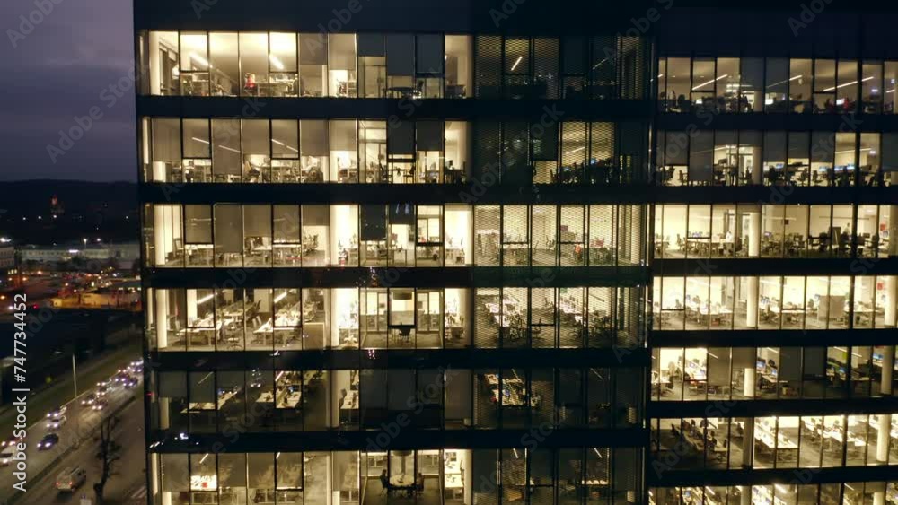 Modern office building at night. Aerial view of the windows of a multi-story skyscraper building made of glass, office lighting and people working until late in the evening inside. Modern office building at night. Aerial view of the windows of a multi-story skyscraper building made of glass, office lighting and people working until late in the evening inside.