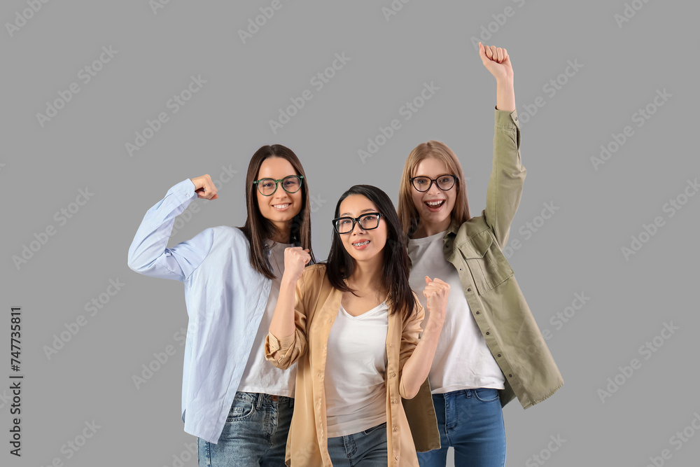 Obraz premium Beautiful young happy women with clenched fists on grey background. Women history month