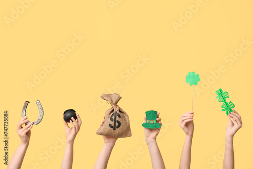 Female hands holding different party decor for St. Patrick's Day celebration on yellow background