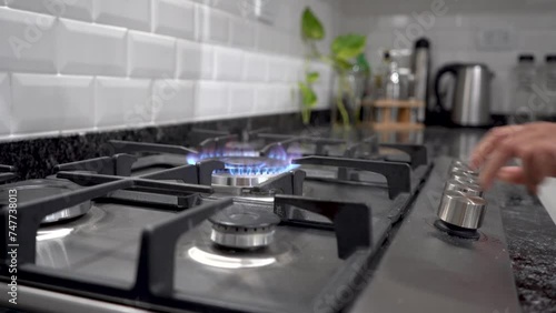 Mano de mujer encendiendo hornalla grande doble corona de estufa a gas natural en contexto de cocina moderna photo