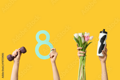 Female hands with paper figure 8, sports equipment and tulips for International Women's Day on yellow background photo
