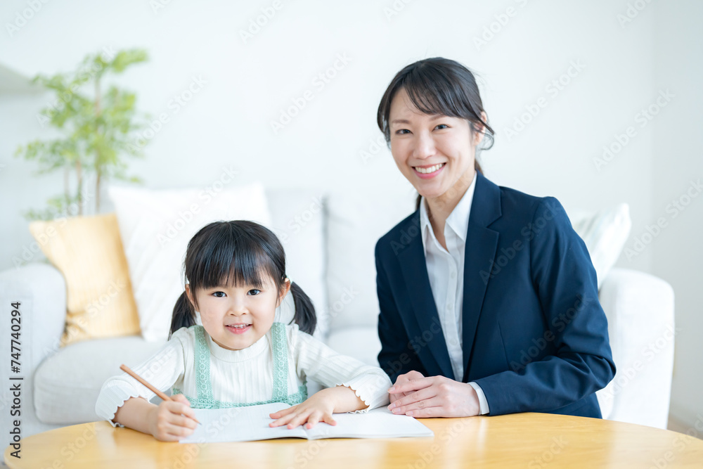 部屋で子供に勉強を教えるスーツを着た女性 部屋で子供に勉強を教えるスーツを着た女性