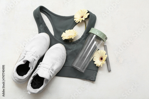 Composition with sports bra, shoes, bottle of water and flowers on light background. International Women's Day photo
