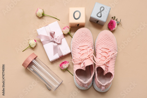 Composition with sports shoes, bottle of water, gift box and flowers on color background. International Women's Day