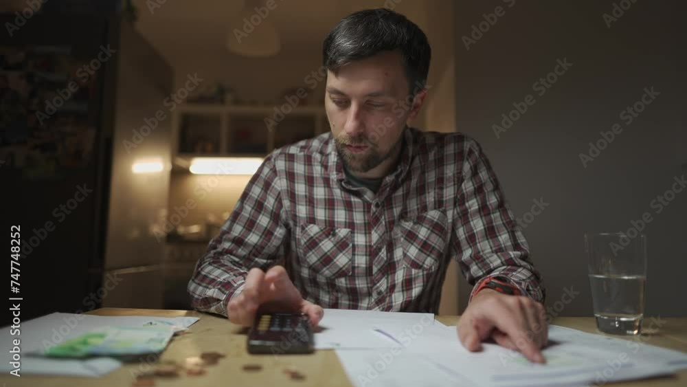 Man checking home finance. Stressed out man pays bills, keeps count of finances on calculator, bank documents expenses and payments at home. Troubled male inspects his household invoices domestically Man checking home finance. Stressed out man pays bills, keeps count of finances on calculator, bank documents expenses and payments at home. Troubled male inspects his household invoices domestically