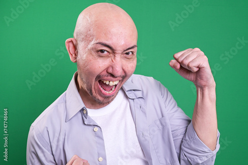 Portrait of satisfied bald man celebrating success over green background