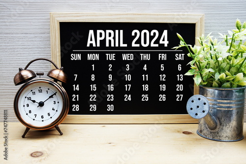 April 2024 monthly calendar and alarm clock on wooden background