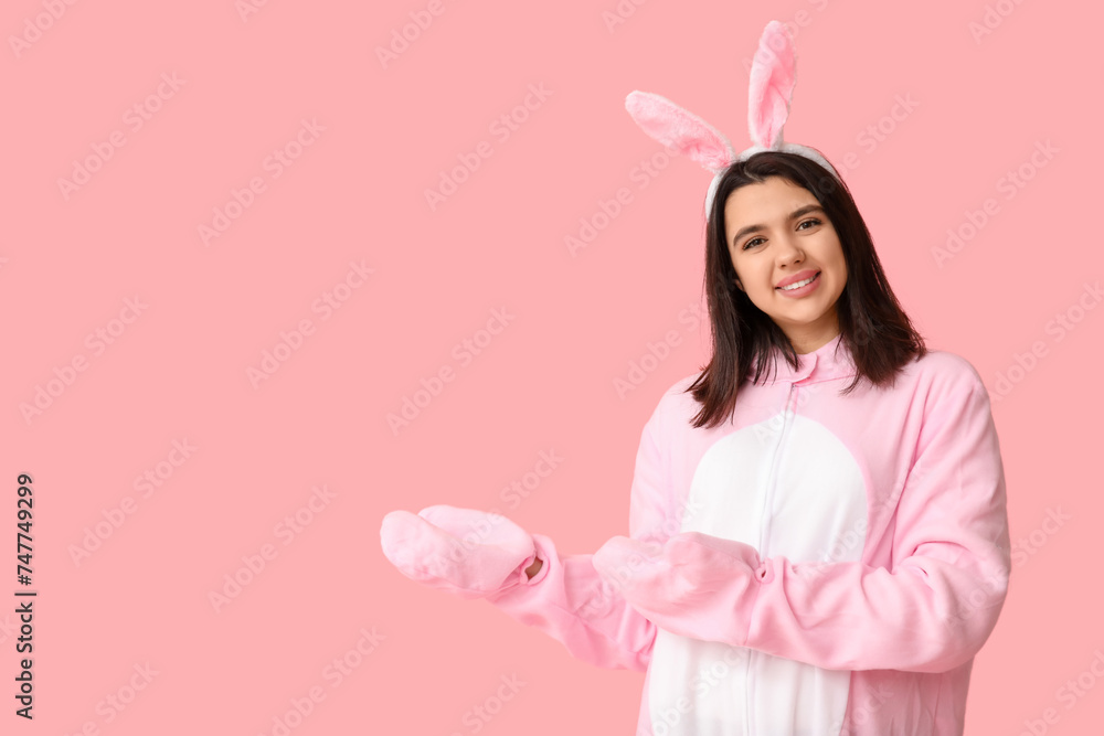 Beautiful young woman in bunny costume pointing at something on pink background. Easter celebration Beautiful young woman in bunny costume pointing at something on pink background. Easter celebration
