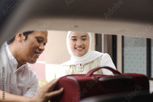 Muslim couple moving the suitcases into the trunk of the car, ready to go on holiday. Mudik lebaran at Eid moment. © Gatot