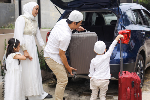 Muslim family moving the suitcases into the trunk of the car, ready to go on holiday. Mudik lebaran at Eid moment.